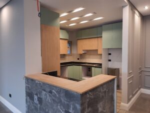 Modern kitchen design by Alpha featuring light wood and mint green cabinetry with a stylish bar counter and LED ceiling lights.